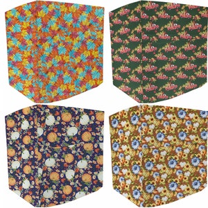 May include: Four different fabric designs featuring autumnal themes. The first design features a pattern of colorful fall leaves on a light orange background. The second design features a pattern of red pickup trucks carrying pumpkins on a dark green background. The third design features a pattern of white pumpkins and small flowers on a dark blue background. The fourth design features a pattern of white pumpkins and blue flowers on a brown background.