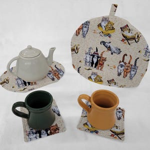 May include: Set of four beige fabric coasters with a cat design. The coasters feature a variety of cats in different poses, including lounging, playing, and sleeping. The coasters are perfect for protecting your furniture from hot drinks.