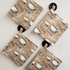 May include: Four brown fabric pot holders with a coffee cup and coffee bean pattern. The pot holders have a black button on the top.