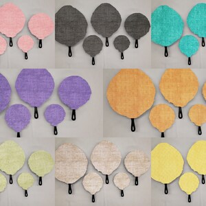 May include: Set of five fabric wall decor pieces in various colors, including pink, gray, teal, purple, orange, yellow, green, and beige. Each piece is a round, flat, fabric circle with a black handle on the back.