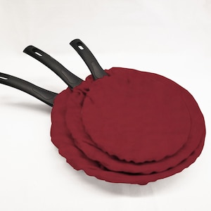 May include: Three red fabric pan protectors stacked on top of each other. The pan protectors are round and have black handles.