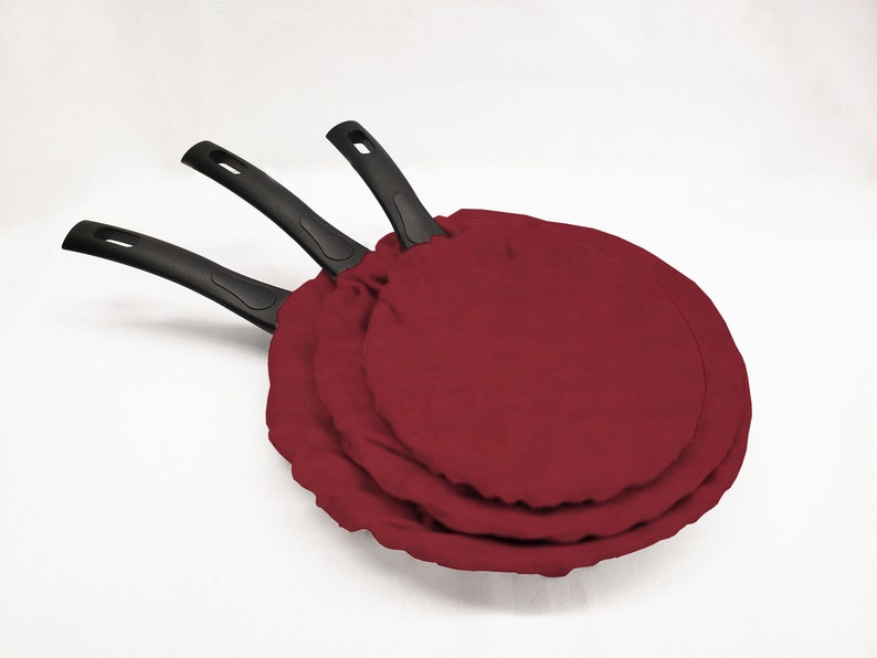 May include: Three red fabric pan protectors stacked on top of each other. The pan protectors are round and have black handles.