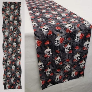 May include: A black and gray table runner with a repeating pattern of white skulls, red roses, and spiderwebs. The runner is approximately 14 inches wide and 72 inches long.