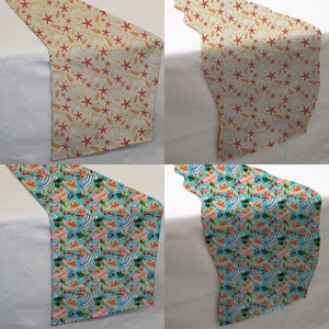 May include: Two table runners with different designs. The first runner has a beige background with red starfish and seashells. The second runner has a blue background with colorful beach hats, palm trees, and striped beach towels.