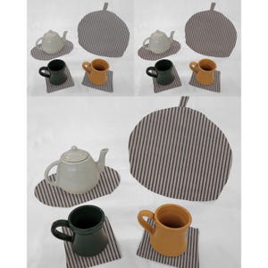 May include: A collection of ceramic teapots, mugs, and tea cozies. The teapots are off-white, the mugs are dark green and mustard yellow. The tea cozies and coasters have a striped pattern. The items are arranged on a white surface.