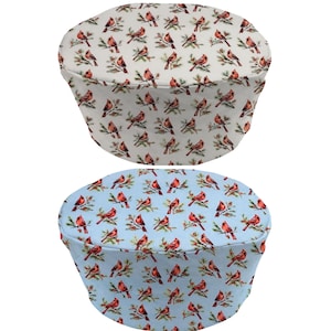 May include: Two round, fabric covers for a small appliance, such as a slow cooker or bread maker. The covers are printed with a pattern of red cardinals on branches. One cover is white with a green background, and the other is light blue with a green background.