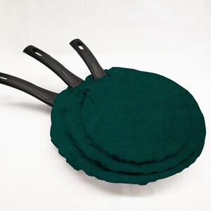 May include: Three black-handled frying pans with dark green fabric covers.
