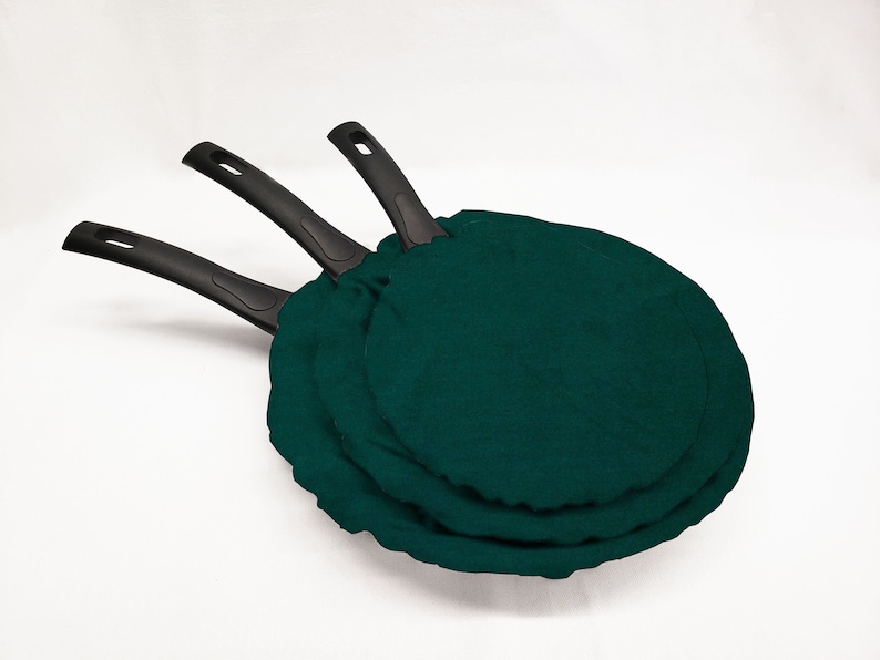 May include: Three black-handled frying pans with dark green fabric covers.