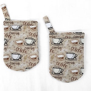 May include: Two beige fabric coffee cup holders with a brown and white coffee cup and coffee bean pattern. The holders have a loop at the top for hanging.