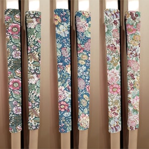 May include: Six floral patterned fabric refrigerator handle covers. The covers are in various colors, including green, blue, and pink. The covers are designed to protect refrigerator handles from scratches and wear.