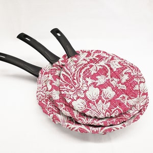 May include: Three nesting frying pans with black handles and a pink and white floral pattern.