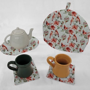 May include: A set of four white ceramic teacups and saucers with a red cardinal and poinsettia design. The set includes a teapot and a tea cozy.