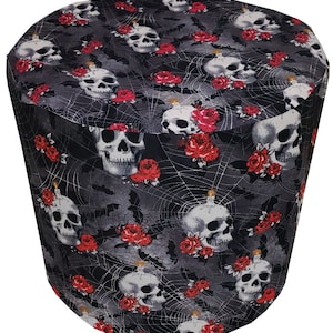 May include: A black and gray fabric item with a repeating pattern of white skulls, red roses, spiderwebs, and bats. The item is cylindrical with a rounded top and is likely a decorative cover.