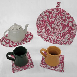 May include: A set of four pink and white floral tea coasters with a matching teapot cozy. The coasters and cozy feature a white floral pattern on a pink background. The set includes two mugs, one green and one yellow.