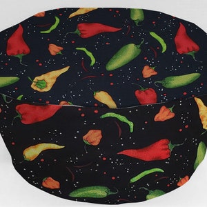 May include: A black fabric hat with a pattern of colorful chili peppers in red, green, yellow, and orange. The peppers are scattered across the hat's surface, with small white dots adding detail. The hat is likely for cooking or food preparation.