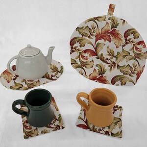 May include: Set of four fabric tea coasters with a floral pattern in shades of green, red, and gold. The coasters are designed to protect surfaces from heat. The set includes a larger coaster for a teapot.