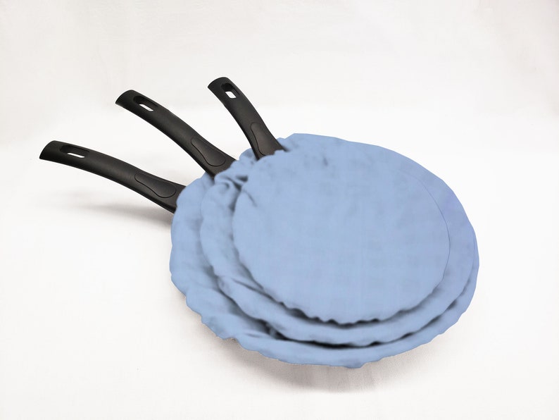 May include: Three black-handled frying pans with blue fabric covers. The pans are stacked on top of each other.