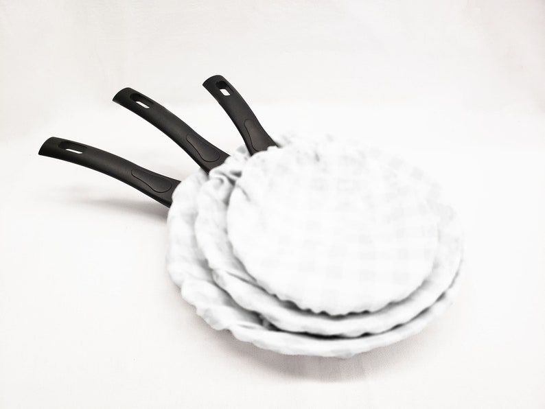 May include: Three black-handled frying pans with white nonstick coating. The pans are stacked on top of each other.