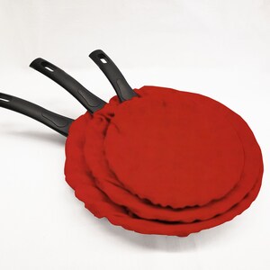 May include: Three black frying pans with red fabric covers. The pans are nested inside each other.