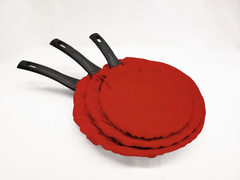 May include: Three black frying pans with red fabric covers. The pans are nested inside each other.