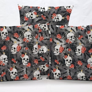May include: Three decorative throw pillows with a black and gray background featuring a repeating pattern of white skulls, red roses, and spiderwebs.