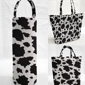 May include: A collection of cow-print tote bags and a wine bottle carrier. The bags have black spots on a white background. The tote bags have handles, and the wine carrier has a single handle.