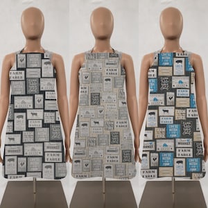 May include: Three black and white aprons with a farmhouse theme. The aprons feature a variety of text, including "Farm Table", "Life is Better on the Farm", and "Fork in the Road".
