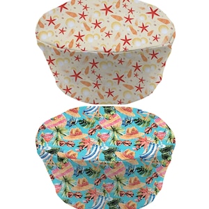May include: Two round chair seat covers. One is beige with orange starfish and seashells. The other is blue with tropical leaves, sunglasses, and cocktails.