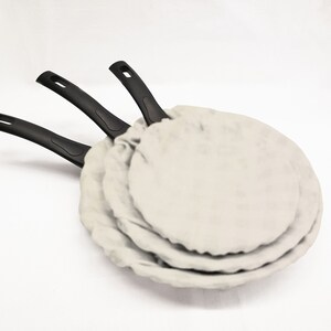May include: Three black handled frying pans with white fabric covers stacked on top of each other.