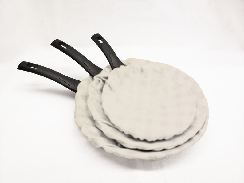 May include: Three black handled frying pans with white fabric covers stacked on top of each other.