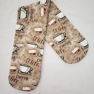 May include: A pair of brown oven mitts with a coffee cup and coffee bean pattern. The mitts are made of a soft, quilted fabric and are perfect for protecting your hands from heat while cooking or baking.