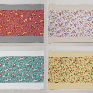 May include: Four fabric table runners with a floral pattern. The runners have a solid color border and a floral pattern in the center. The colors of the runners are pink, white, teal, and yellow.