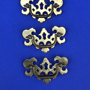 May include: Three ornate metal drawer pulls with a decorative, openwork design. The pulls are a light gold color with a dark brown finish.