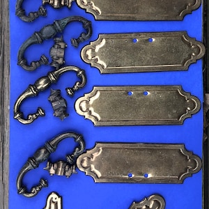 May include: A set of antique brass cabinet hardware, including drawer pulls and plates. The hardware is in various styles and sizes, with some pieces having a decorative floral design.