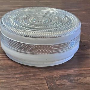 May include: A clear glass, round light fixture with a frosted bottom and a decorative, textured design. The top features a spiral pattern, and the sides have a patterned band. The fixture is likely for a ceiling or wall.