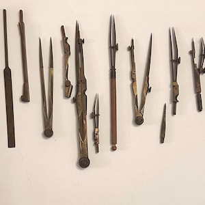 May include: A collection of antique metal drafting tools and compasses arranged next to a wooden ruler measuring 10 inches. The set includes various dividers, scribers, and precision instruments with brass and steel components, showing signs of age.