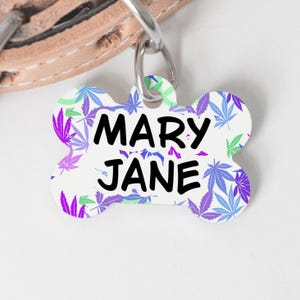 May include: White bone-shaped dog tag with a purple, blue, and green marijuana leaf pattern. The text "MARY JANE" is printed in black.