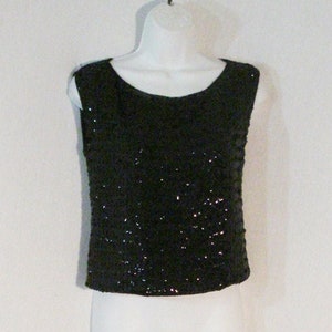 May include: A black sleeveless top with a sequined design. The top is hanging on a white mannequin.