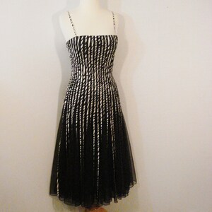 May include: A black and white striped sleeveless dress with a fitted bodice and a flowing skirt. The dress is made of a sheer fabric and has a simple, elegant design.