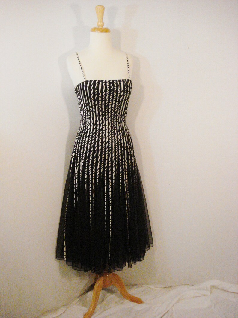 May include: A black and white striped sleeveless dress with a fitted bodice and a flowing skirt. The dress is made of a sheer fabric and has a simple, elegant design.