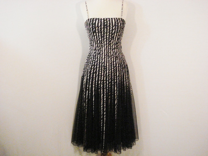 May include: A black and white striped sleeveless dress with a black tulle overlay. The dress has a fitted bodice and a flowing skirt.
