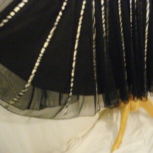 May include: Black tulle skirt with white trim. The skirt is gathered at the waist and has a flowing silhouette.