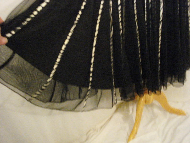 May include: Black tulle skirt with white trim. The skirt is gathered at the waist and has a flowing silhouette.