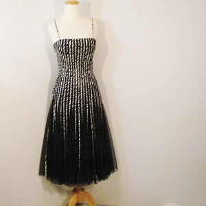 May include: A black and white striped sleeveless dress with a fitted bodice and a flowing skirt. The dress is made of a sheer fabric and has a delicate, feminine look.