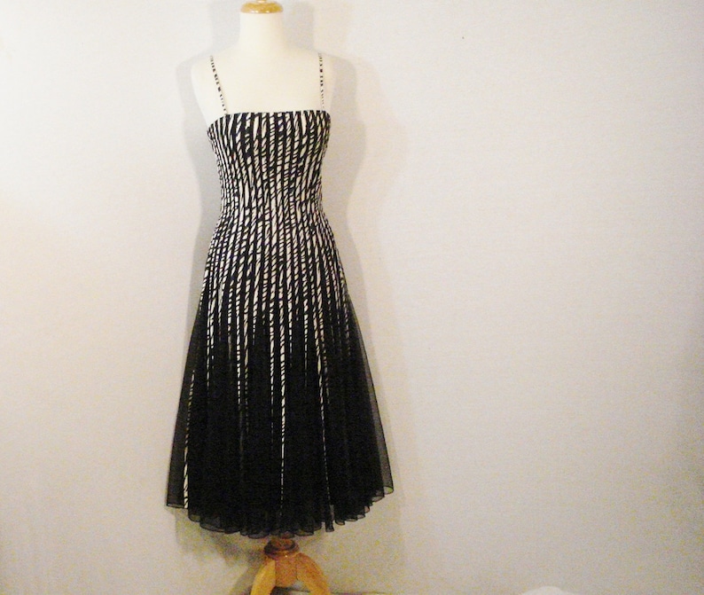 May include: A black and white striped sleeveless dress with a fitted bodice and a flowing skirt. The dress is made of a sheer fabric and has a delicate, feminine look.