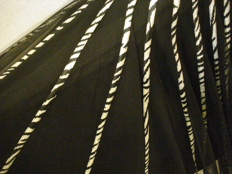 May include: Black and white striped fabric with a sheer texture. The fabric is gathered in a fan shape, creating a layered effect.