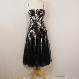May include: A black and white striped dress with a black tulle skirt. The dress is on a wooden mannequin.