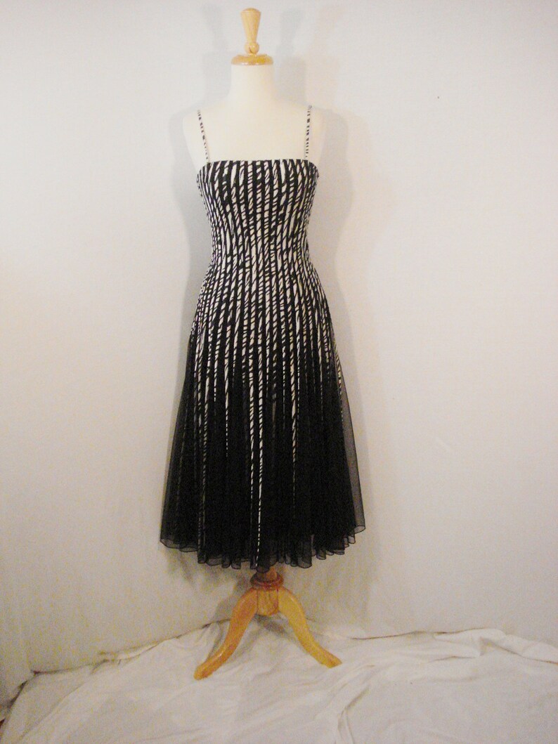 May include: A black and white striped dress with a black tulle skirt. The dress is on a wooden mannequin.