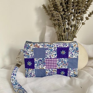 May include: A patchwork clutch bag with a wrist strap. The bag features a variety of blue floral and polka dot patterns, with a purple gingham square. The wrist strap and zip are a matching blue floral pattern.