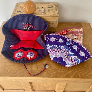 Puede incluir: Una colección de accesorios de costura, que incluye un estuche para agujas a rayas azul marino con detalles rojos, tijeras y un portahilos de madera en forma de huevo. También, una pequeña caja de madera y dos bolsas de tela.
